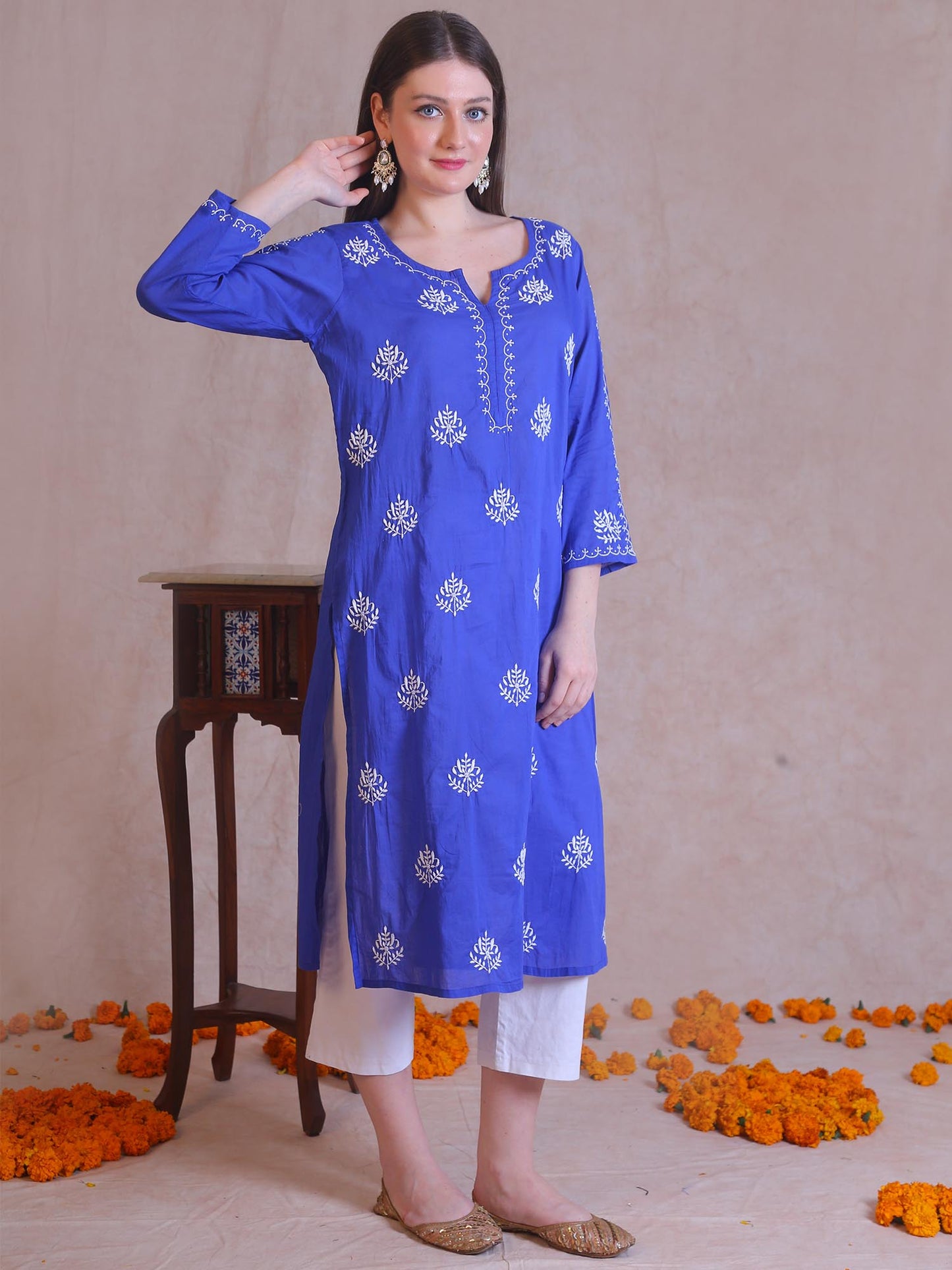 Woman wearing a blue embroidered kurta with white pants against a beige background.