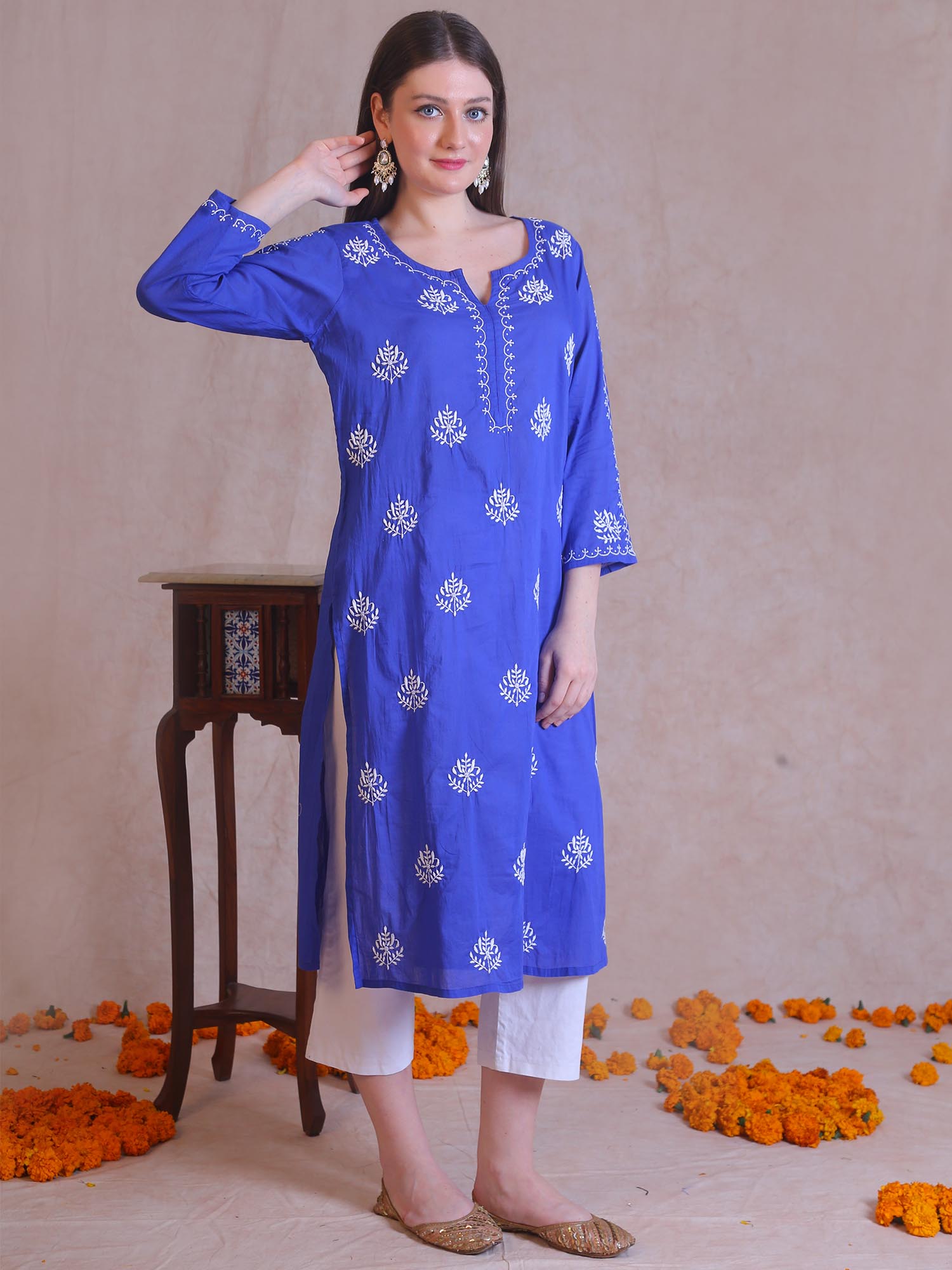 Woman wearing a blue embroidered kurta with white pants against a beige background.